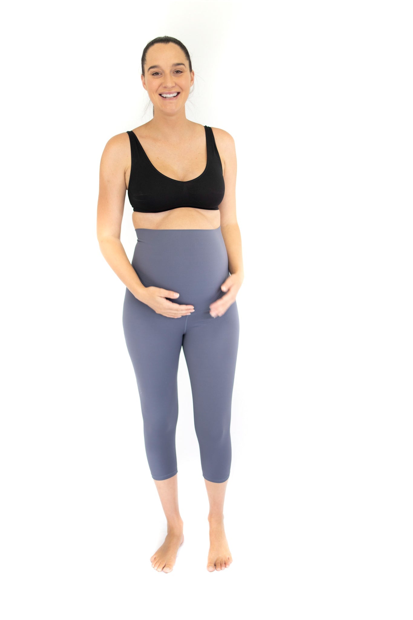 Smiling pregnant woman in black sports bra and blue 3/4 maternity leggings - Twilight