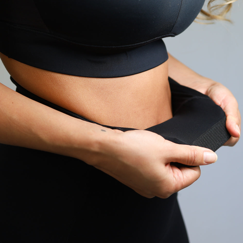 Midriff-baring black athletic outfit being adjusted, introducing Emamaco shapewear