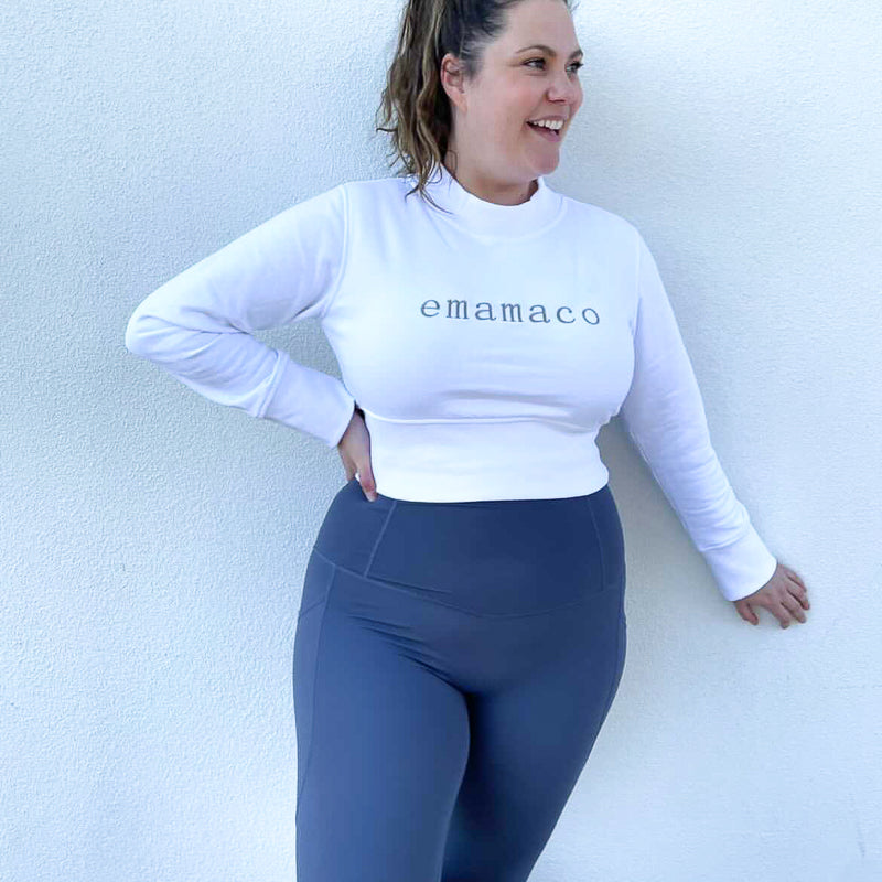 Woman in white cropped sweatshirt with Emamaco text and blue leggings in shapewear