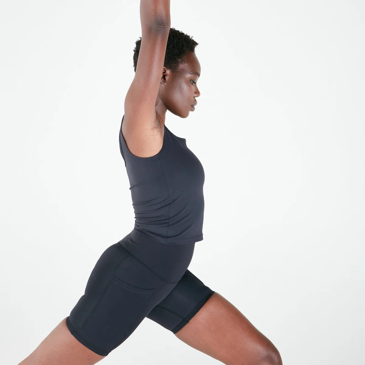 Woman in dark athletic wear stretching, showcasing Emamaco Everyday Singlet in yoga studio