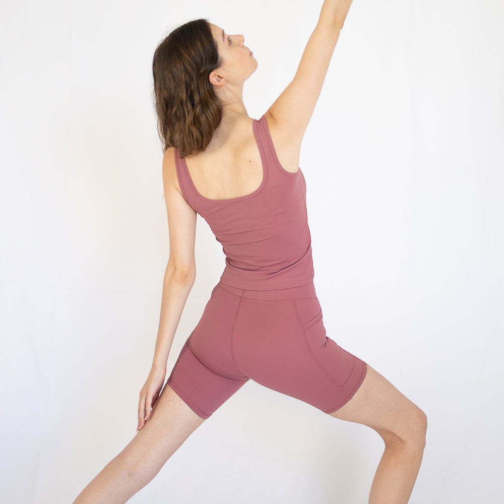 Woman in a pink workout outfit poses confidently in Emamaco Everyday Singlet in yoga studio