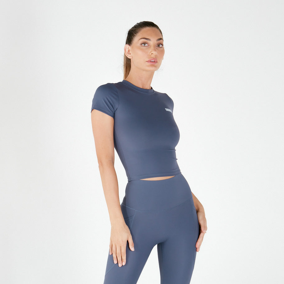 Woman in fitted blue-gray athletic crop top and leggings made of Supaflex material