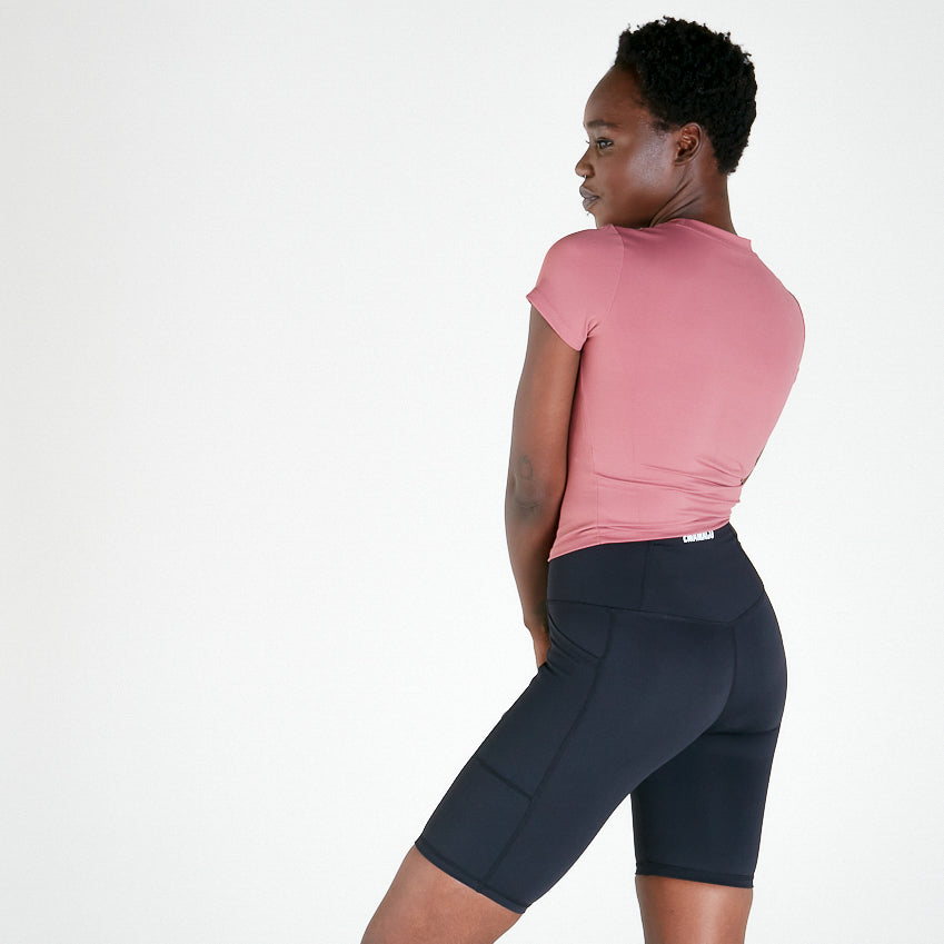 Woman in pink t-shirt and dark cycling shorts showcasing Vibe V Long Shorts in Black